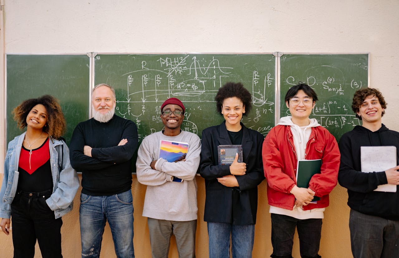 A diverse group of students and a teacher smiling in front of a chalkboard filled with formulas.